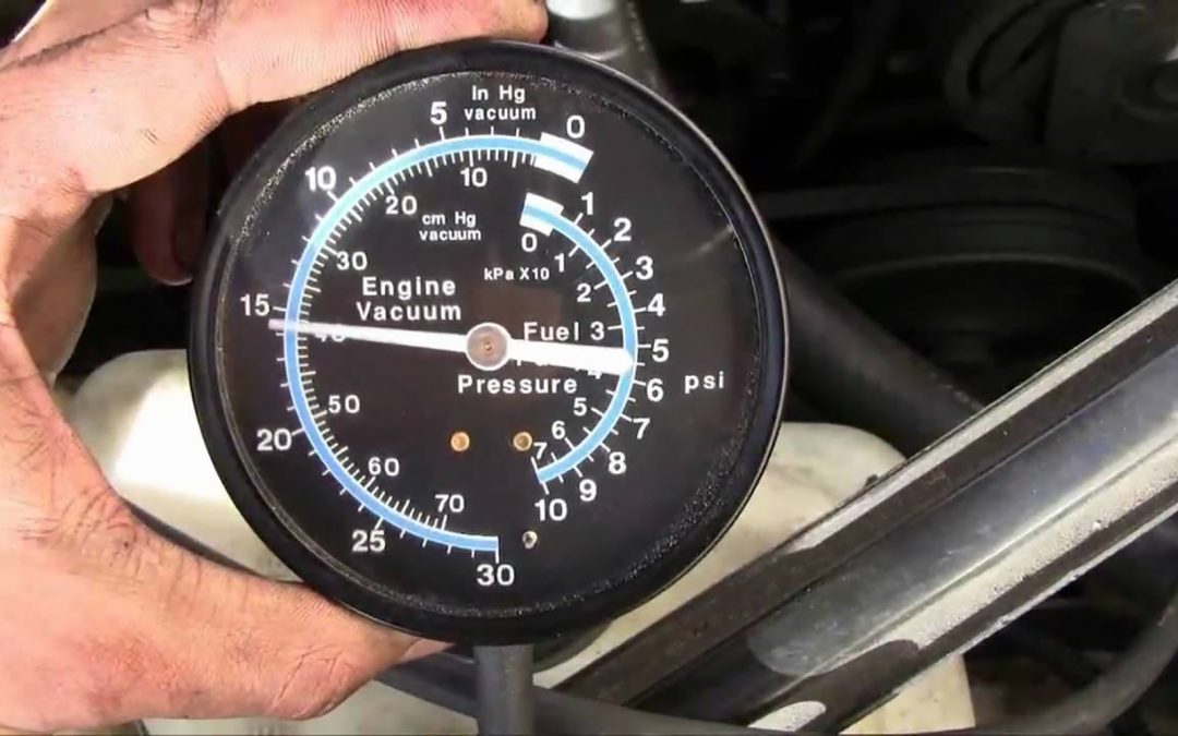 Man holding a vacuum gauge testing the vacuum on a vehicle to diagnose a hard brake pedal.